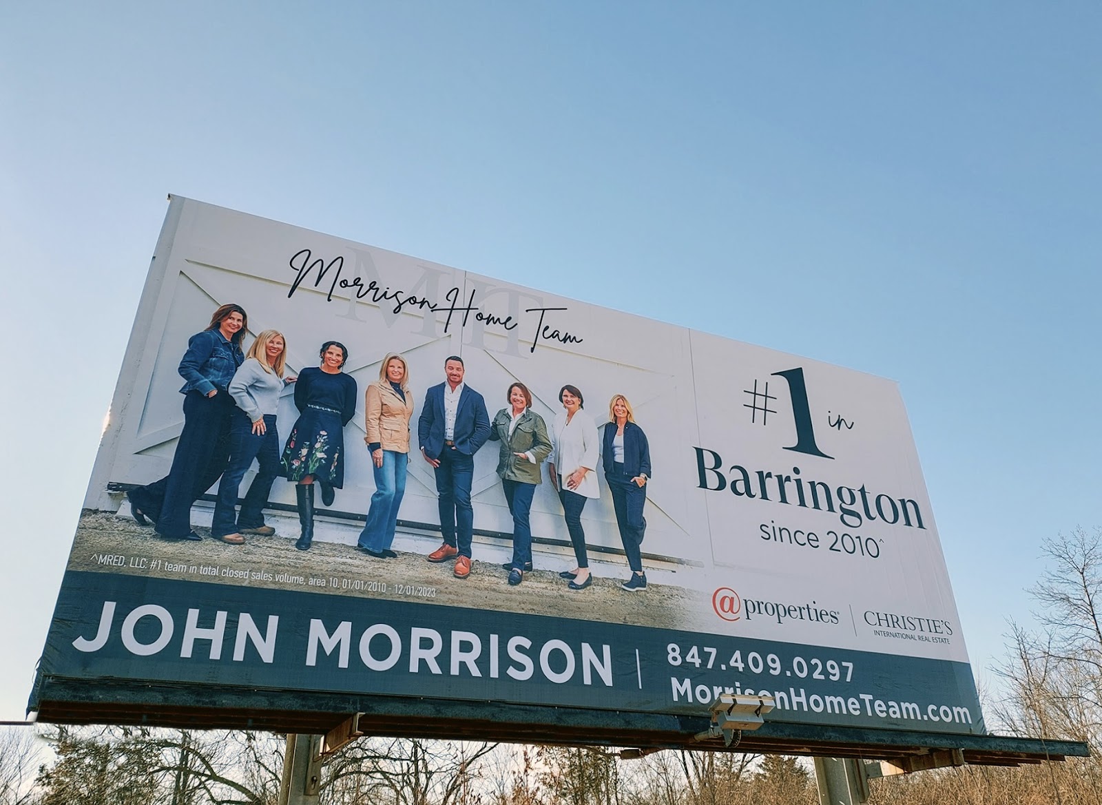 Large roadside billboard showing a real estate team photo and contact details