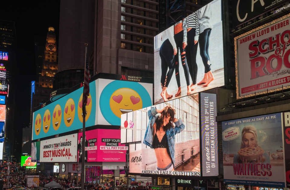 Nighttime view of Times Square filled with illuminated digital billboards promoting Broadway shows, fashion brands, and entertainment campaigns.