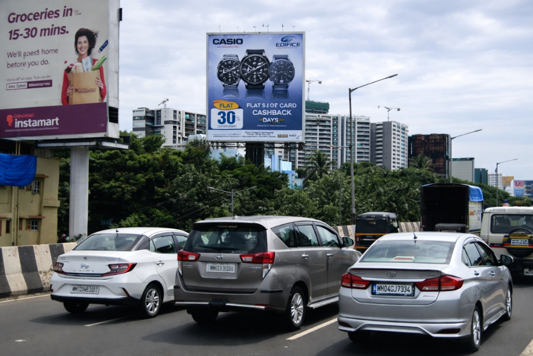 Casio Edifice watch billboard above traffic, with an Instamart advertisement on a nearby hoarding