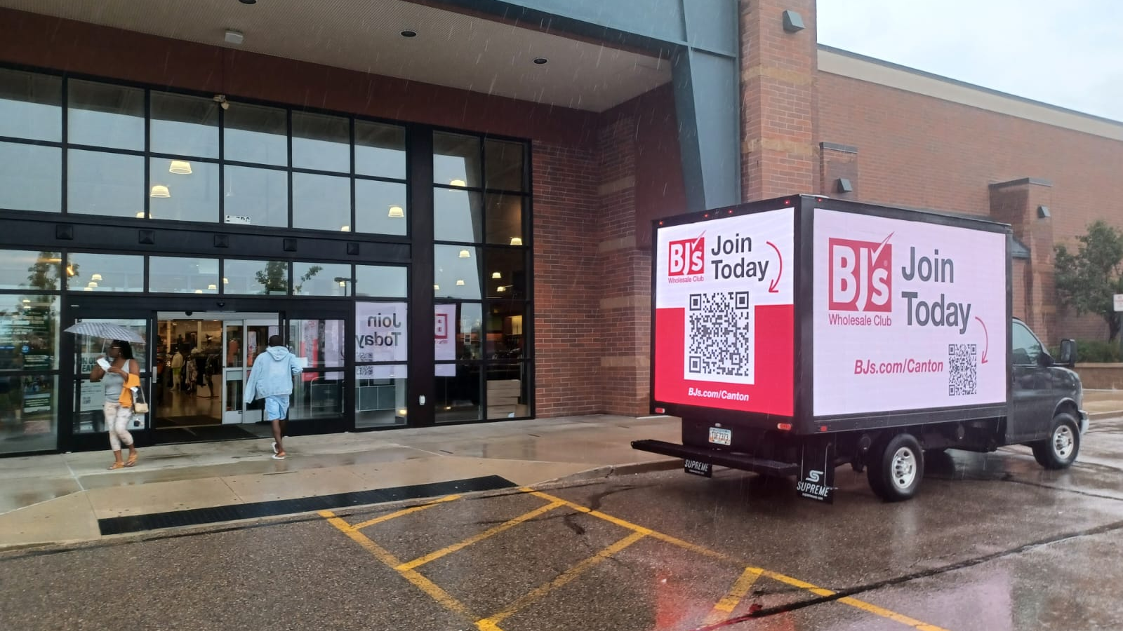 BJ’s Wholesale Club mobile digital billboard truck parked outside a retail store entrance in rainy weather.