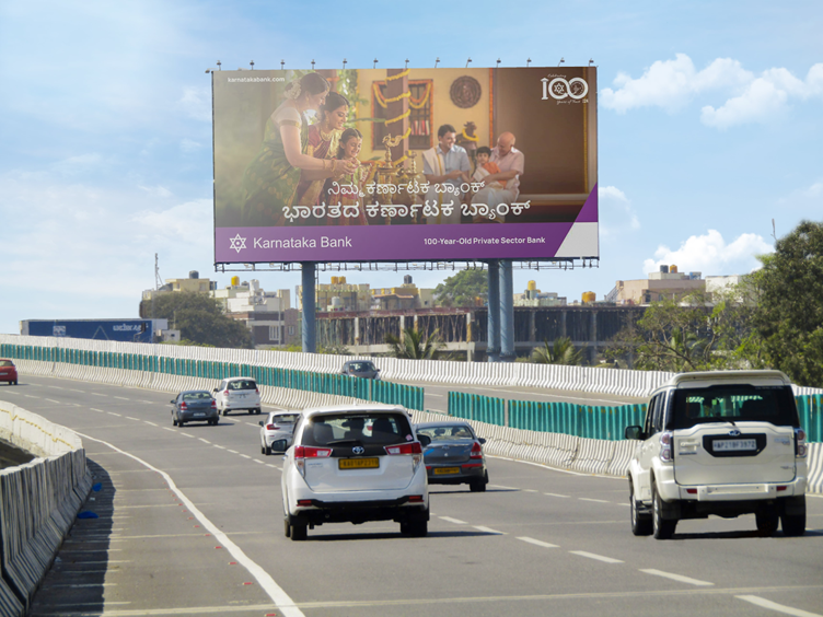 Karnataka Bank roadside billboard displayed along a highway with moving traffic