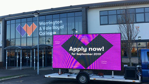 Mobile LED screen truck displaying “Apply now” message parked outside Warrington & Vale Royal College for admissions promotion.