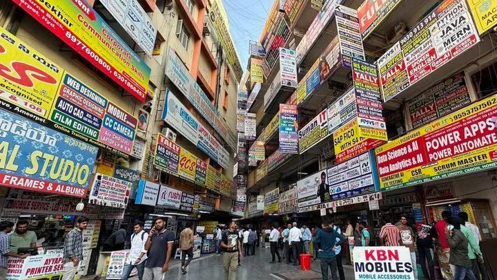 Busy marketplace street filled with numerous signboards and advertisements for coaching institutes and training centers.