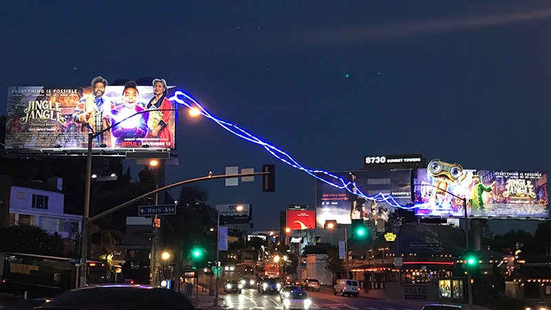 Nighttime billboard campaign with interactive light effect connecting two hoardings across a busy street