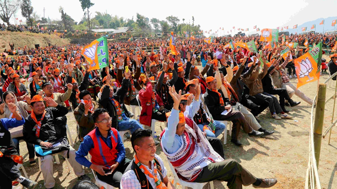 Large crowd of BJP supporters waving saffron party flags and lotus symbols at an outdoor election rally in Northeast India