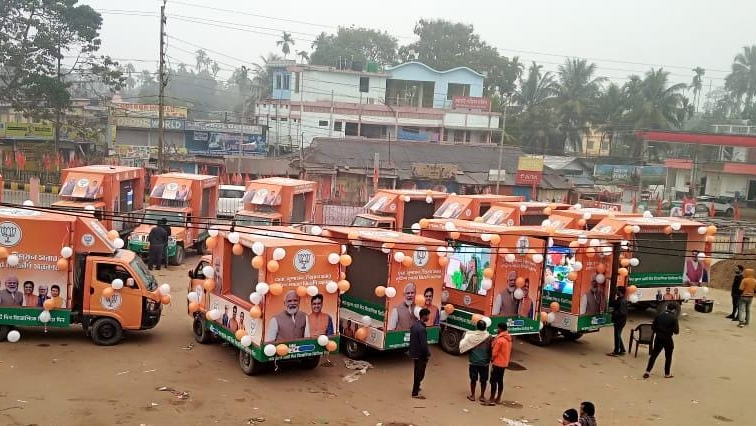 Fleet of saffron-colored BJP campaign vehicles decorated with party flags and balloons lined up in a town square in India