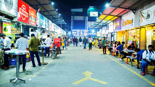Street food market scene representing local consumer culture and footfall Busy street food market with multiple food stalls and customers dining in urban night setting