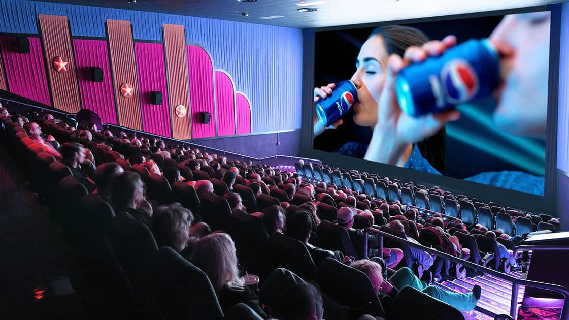 Crowded cinema auditorium where audiences watch a large screen advertisement featuring a beverage brand before the movie.