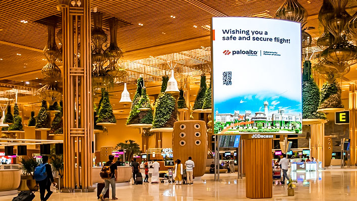 Large vertical digital advertising screen inside an airport terminal displaying a Palo Alto Networks message wishing travelers a safe flight.