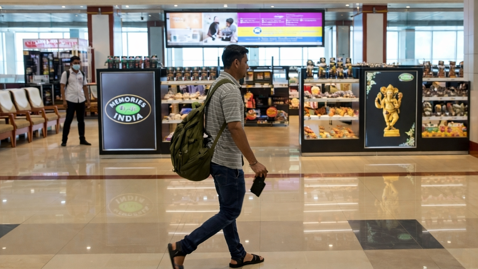 Airport retail area featuring illuminated digital displays for “Memories of India” gift store with passengers walking nearby.