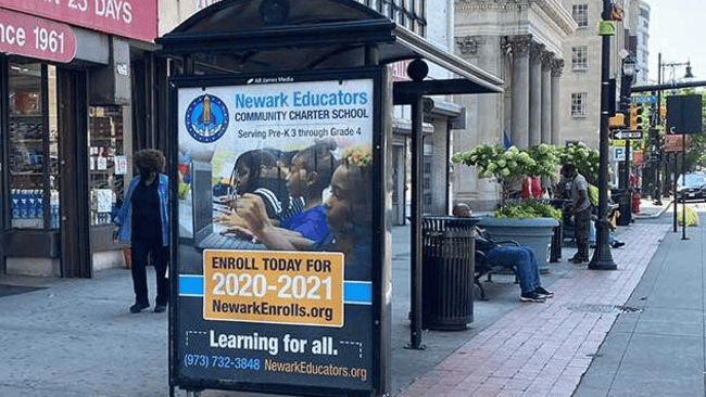 Bus shelter advertising panel promoting Newark Educators Community Charter School enrollment for the academic year.