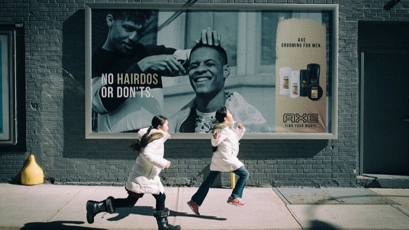 Street billboard advertisement by Axe featuring men’s grooming products with “No Hairdos or Don’ts” tagline and children running past urban wall