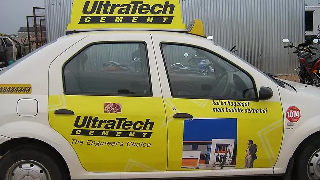 Taxi car branded with UltraTech Cement advertisement featuring product messaging and construction imagery