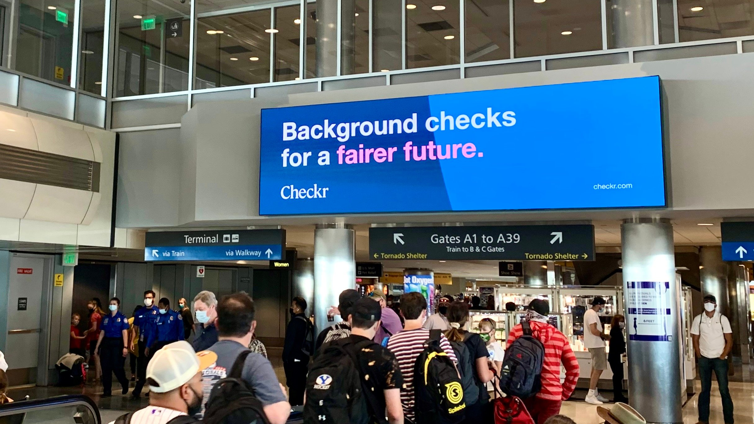 Digital billboard inside airport displaying Checkr background verification campaign with passengers walking below