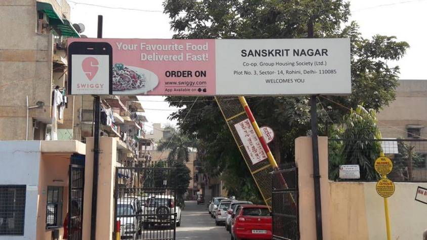 Residential society entrance gate featuring Swiggy advertisement promoting fast food delivery service
