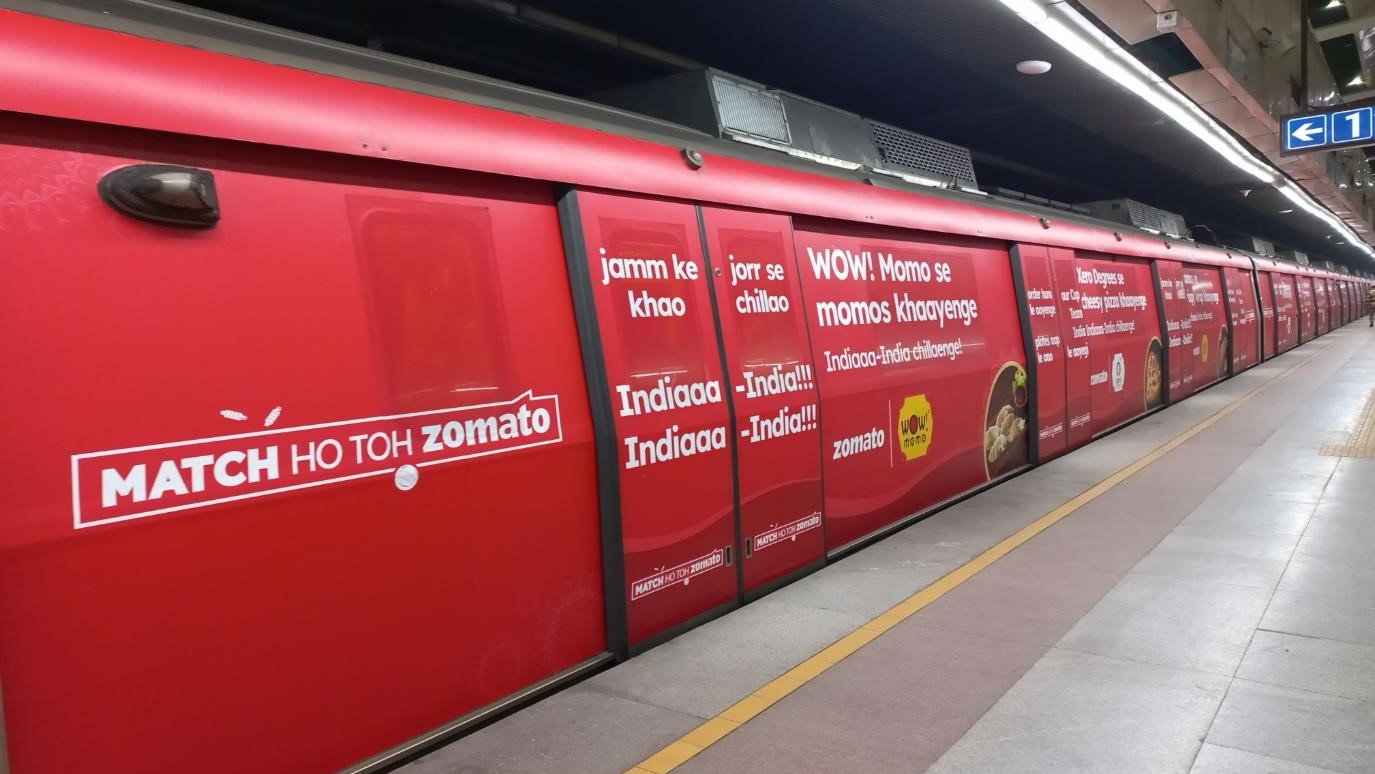 Full metro train branding by Zomato with red creative campaign promoting food delivery and momos messaging