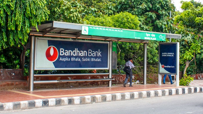 Bus shelter advertising by Bandhan Bank with branding panel and pedestrian waiting area on roadside